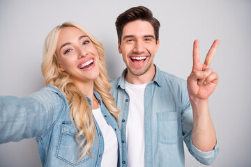 Photo of young cheerful couple happy positive smile show peace cool v-sign shoot selfie isolated over grey color background