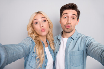 Photo of pretty charming young couple dressed jeans shirts tacking selfie sending you kiss isolated grey color background