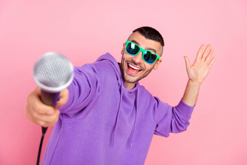 Photo of cute young brunet guy hold mic wear eyewear hoodie isolated on pink background