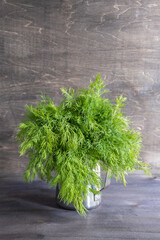 A bunch of dill in a small pitcher with water on a natural dark wooden background.