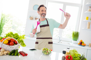 Photo of cheerful carefree age man dressed blue t-shirt apron smiling cooking salad dancing indoors home room