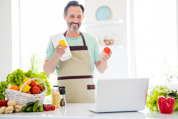 Photo of good mood cheerful age man dressed blue t-shirt apron smiling cooking watching modern gadget indoors home room