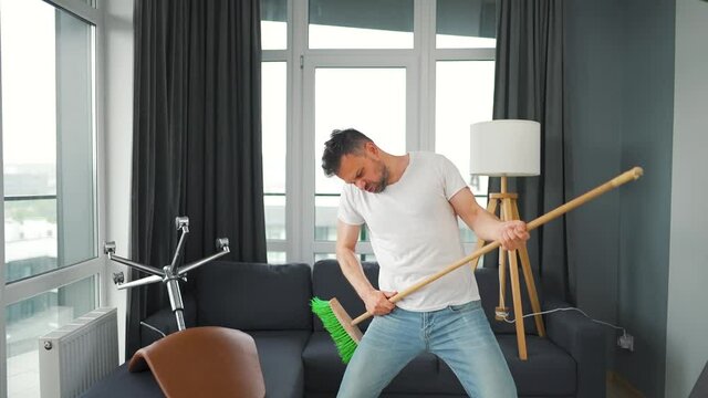 Man does the cleaning and imagines himself a rock star, plays the broom like a guitar. Slow motion