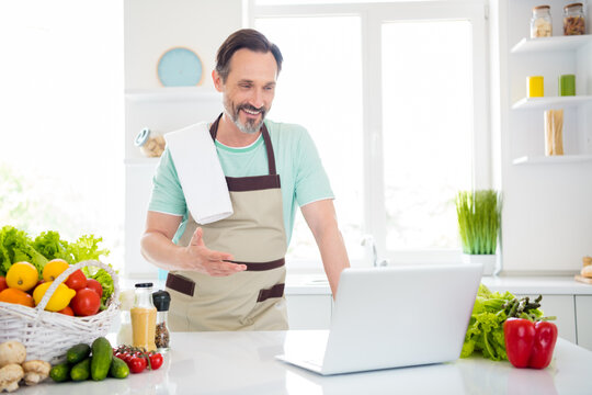 Photo of confident nice man look screen laptop video call lesson wear apron blue t-shirt home kitchen indoors