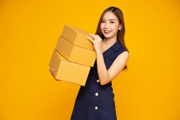 Happy Asian woman smiling and holding package parcel box isolated on yellow background, Delivery courier and shipping service concept