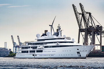 Super yacht at the port of Hamburg with cranes of a container terminal