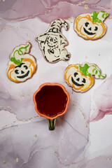 Halloween creative concept: pumpkin cup and homemade cookies in shape of cute pumpkins and ghost closeup. Aesthetic autumn mood or trick or treat concept. Autumn cozy home concept.