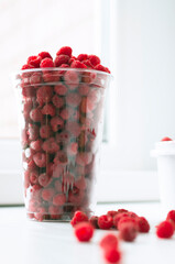 Ripe raspberries in a transparent glass. Ripe raspberries on a white background. Juicy ripe berries.
