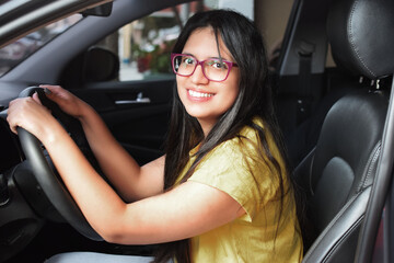 Fototapeta na wymiar Chica joven latina feliz y sonriente, sentada en su automóvil nuevo. Mujer Joven conduciendo.