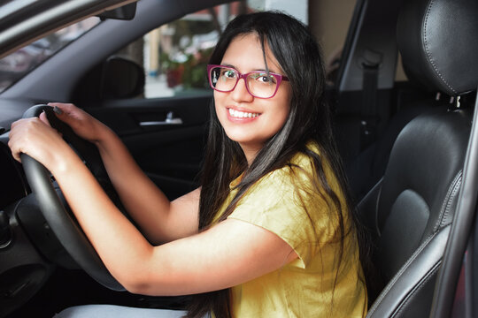 Chica joven latina feliz y sonriente, sentada en su autom&oacute;vil nuevo. Mujer Joven conduciendo.