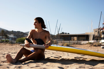 Portrait of handsome surfer with his surfboard. Young man with a surfboard on the beach..