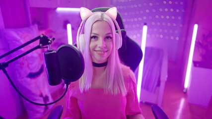 Cute smiling Gamer Girl with cat ear headphones in pink room stare in camera