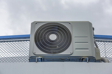 External box of an old air conditioner with a fan against a cloudy sky
