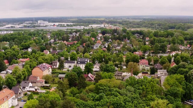 Aerial photos flying over Neuenhagen, a small town in Germany in the federal state of Brandenburg. You can see many green trees, small houses and in the background you can see an industrial area.