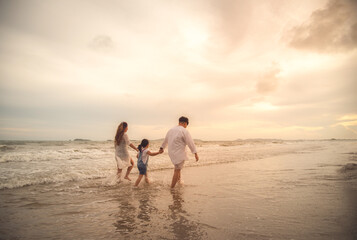 Fototapeta na wymiar Happy family on the beach against blue sea and sky background at sunset. Holiday and summer travel concept