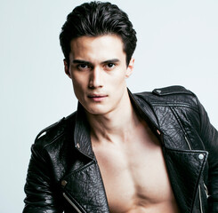 Obraz premium young handsome man, leather jacked on naked torso, emotional posing, white background, modern guy, lifestyle people concept close up
