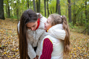 The little sister tells the big one her secrets while walking in the park in the autumn
