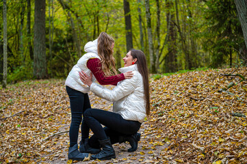 Fototapeta premium two sisters dressed in light jackets walk in the park in autumn, talk and share secrets