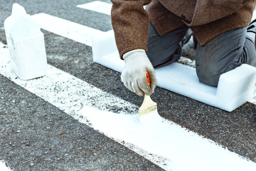 A man paints with a brush on the asphalt markings for a pedestrian crossing. Roadway repair.