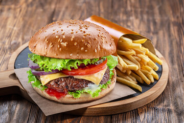 Delicious burger with  potato fries on a wooden table with a dark brown background behind. Fast food concept.
