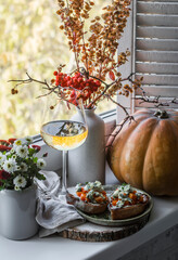 Glass of white wine and pumpkin gorgonzola bruschetta on the windowsill. Autumn still life with chrysanthemums, pumpkin on the background of the window. Autumn mood - obrazy, fototapety, plakaty