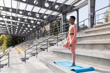 African American woman doing yoga near the stadium in the morning, active lifestyle performs...