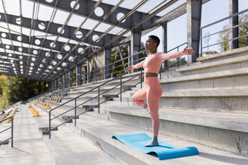 African American woman doing yoga near the stadium in the morning, active lifestyle performs...