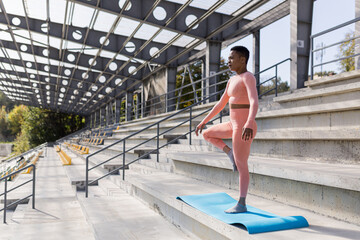 African American woman doing yoga near the stadium in the morning, active lifestyle performs...