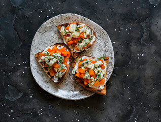 Delicious appetizer, tapas - baked pumpkin, gorgonzola, honey, thyme bruschetta on a dark background, top view