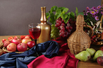 Glass of wine, bottle, grapes and red drapery on the table.
