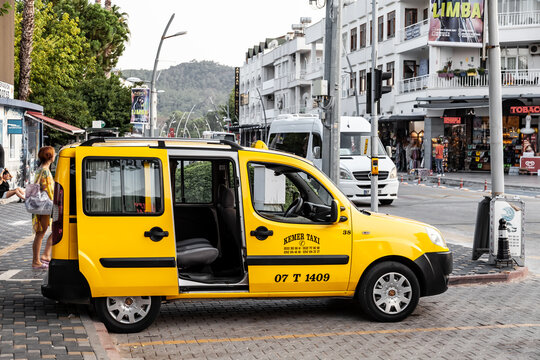 Kemer, Turkey - 08. 25. 2021: yellow taxi Fiat Doblo is parked on the street on a warm summer day against the backdrop of a street, trees