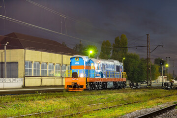 Dnepropetrovsk, Ukraine - Autumn 2021: Shunting diesel locomotive ChME3 painted in the new Ukrzaliznitsa livery stands at a large marshalling yard awaiting work. Night photo.