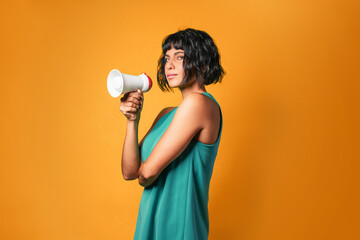 Pretty European woman wearing a teal tank top talking loud on a megaphone against an orange...