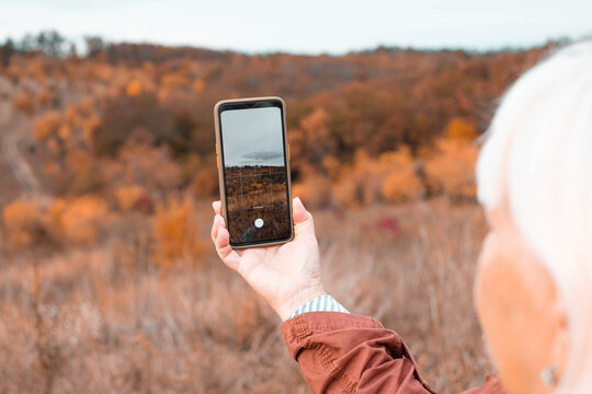 Close up of female tourist hands making a photo with smartphone in a gold autumn park