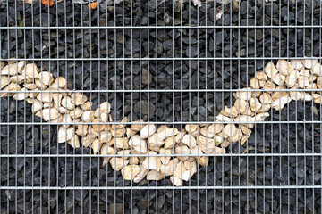 Close up Gabion, metal basket filled with gray and biege granite stones. Stones in steel wire cage