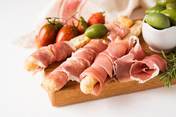 Traditional Italian wine appetizer - breadsticks grissini, prosciutto, jamon, olives and strawberries, close up