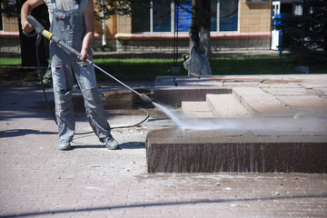 A worker washes dirt from concrete tiles with water under pressure.