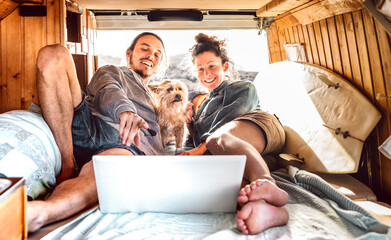 Independent couple with cute dog using laptop on retro mini van transport - Travel life inspiration concept with indie man and woman on minivan adventure trip watching pc on relax moment - Warm filter