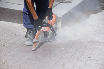 A worker cuts paving slabs laid out in even rows with a circular saw, a lot of dust.
