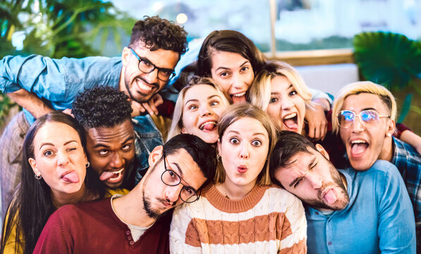 Multicultural men and women taking selfie sticking out tongue with crazy funny faces - Life style and integration concept with interracial young friends having fun together - Indoor lights filter