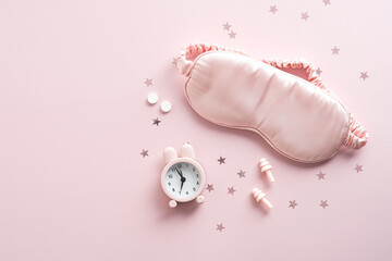 Female eye mask, alarm clock, earplugs, pills on pink background with confetti. Insomnia treatment...