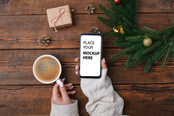 Female hands holding modern smartphone with mockup on wooden vintage table with christmas