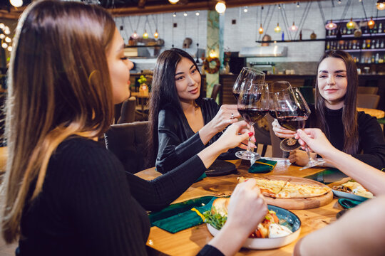 Girls Clink Glasses With Wine At A Dinner In A Restaurant.