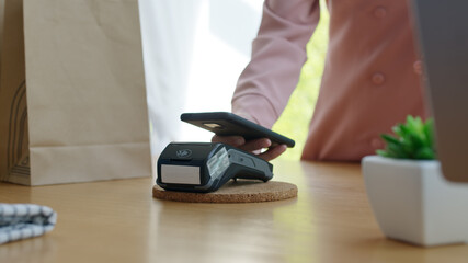 Close-up hand asia woman people work in small sme coffee cafe shop store owner use cashless wifi paywave nfc scan app smart pos reader sale in take out food drink order in urban city life contactless.