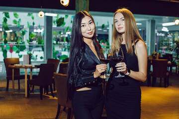 Two girlfriends with glasses of wine stand in a restaurant.
