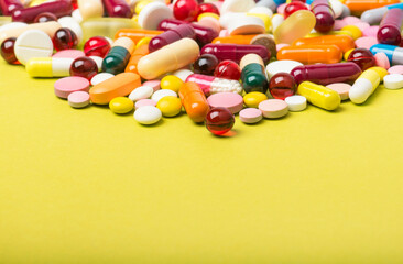 Colorful pills and capsules on yellow background