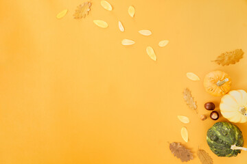 Autumn concept. Foliage with pumpkins and nuts on orange background. Minimal composition with copy space for thanksgiving and halloween.