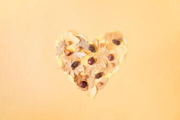 Autumn concept. Fall leaves, chestnuts, pine cones and hazelnuts in a shape of heart on light orange background. Minimal, flat lay.