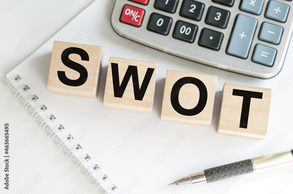 Poster the word of swot on wooden cubes, which lie next to a pen and a calculator on a notebook