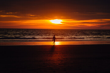 man walking calmly on the beach reflected in the shore with intense sunset of orange and purple colors with soft clouds